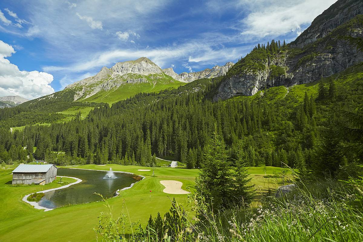 Sunny view of the emerald green golf course in Lech, sand traps & water hazard. showing with the mountains in the background.
