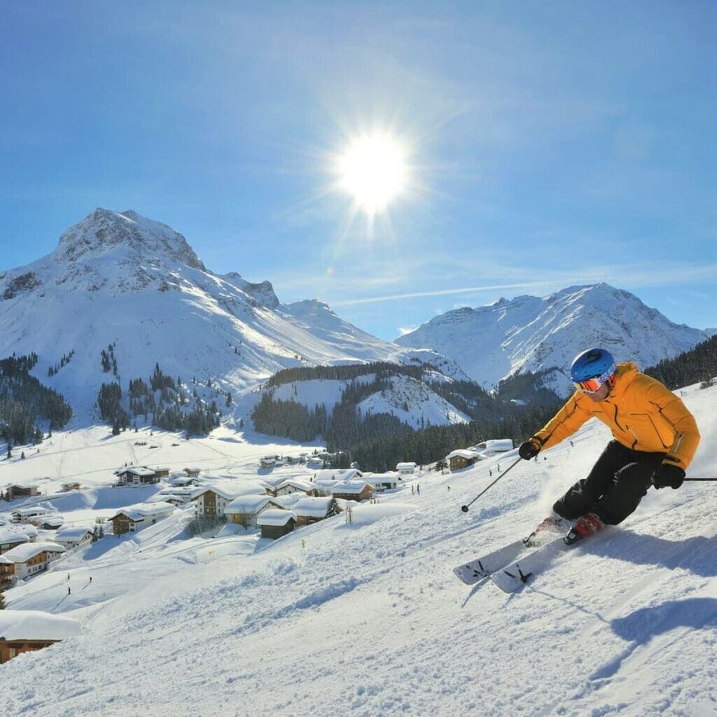 A person with yellow jacket skiing downhill on a sunny day in Lech