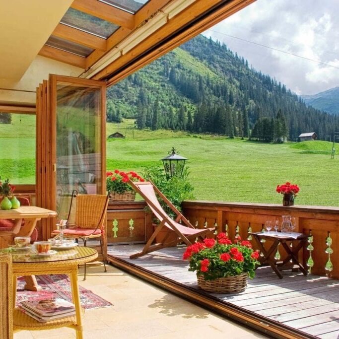 Blick und Perspektive vom offenen Wintergarten des Hotel Alpenland nach Zürs mit einem saftigen grünen Wiesen an einem sonnigen Tag.